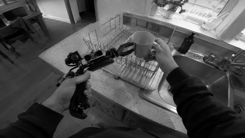 A handheld gripper rig held over a dish rack, recording the task from the wearer's point of view.